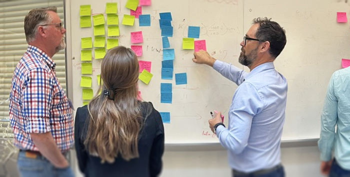 Three people stand in front of a white board filled with sticky notes