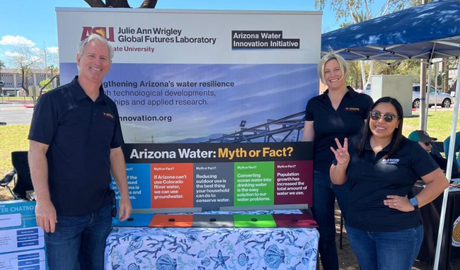 Three people stand smiling in front of a table at a water festival.