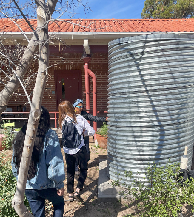 Three people examine a rainwater harvesting catchment set up