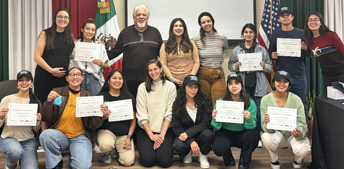 A large group of people hold graduation certificates up for the camera