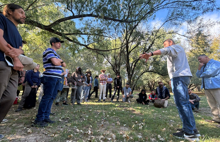 A group of people stand in park listening to a man talking.