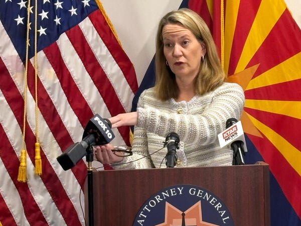 A woman stands in front of microphones at a podium