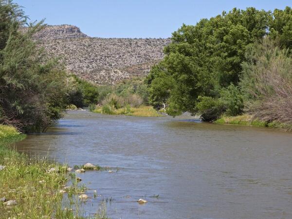 A river flows through a desert landscape at dusk with purple skies overhead.