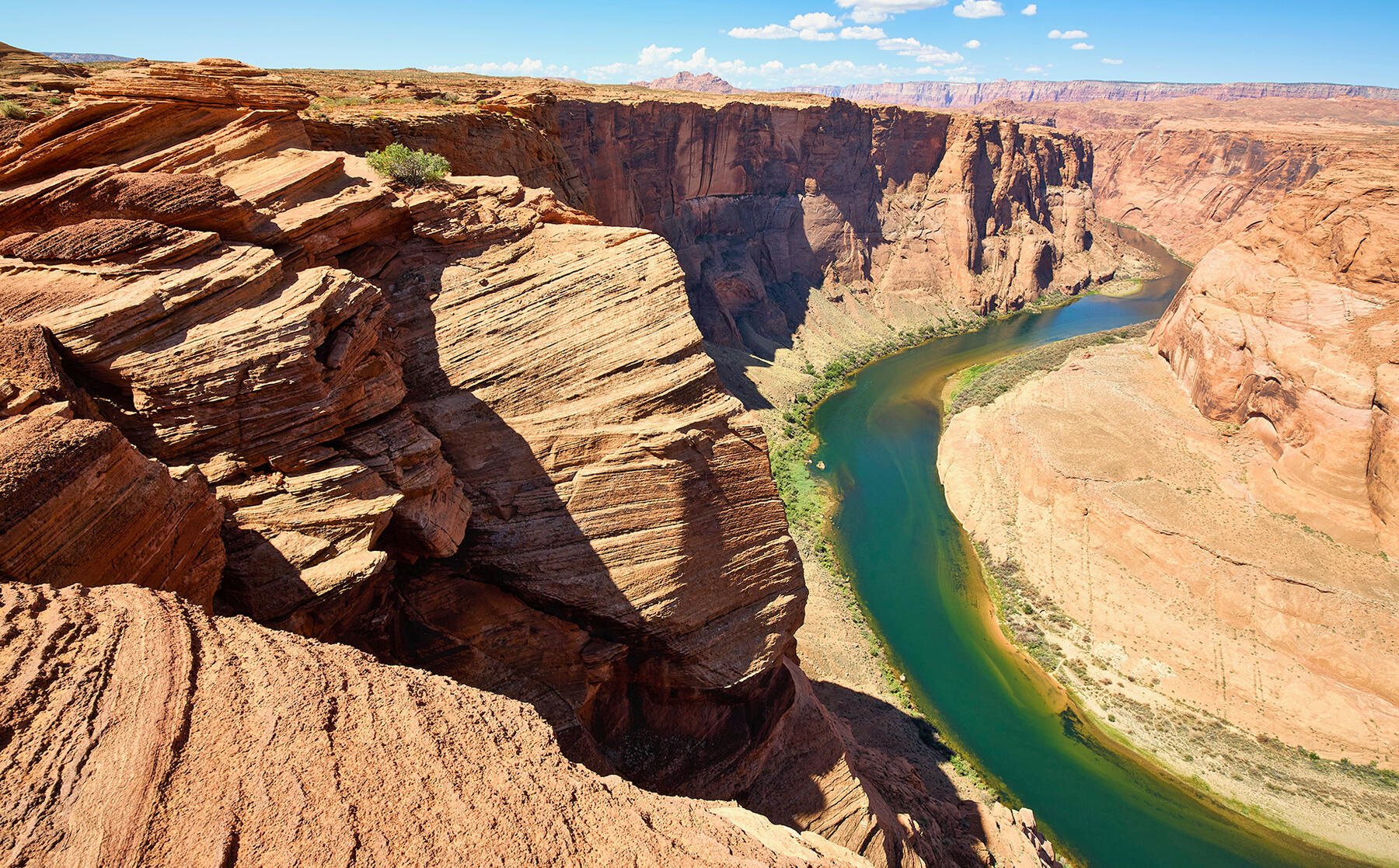 A blue-green ribbon of river flows through the peach and rust colored high canyon walls surrounding it.