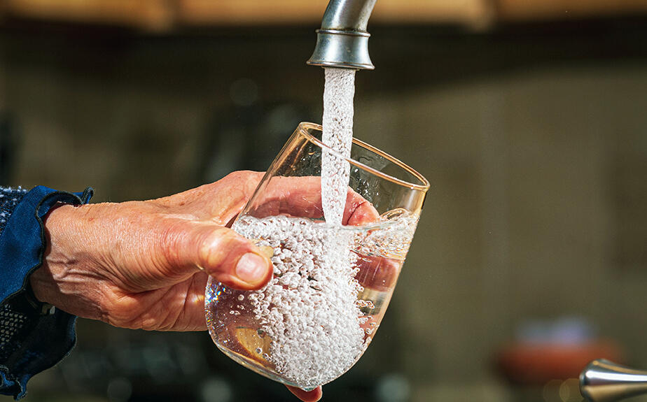 A hand holds a glass under a faucet filling it with water.