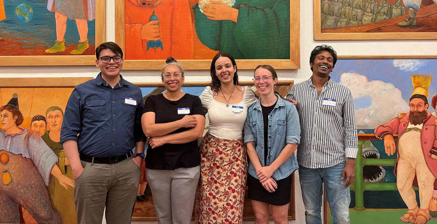 Five people stand side by side in front of a colorful painting display.