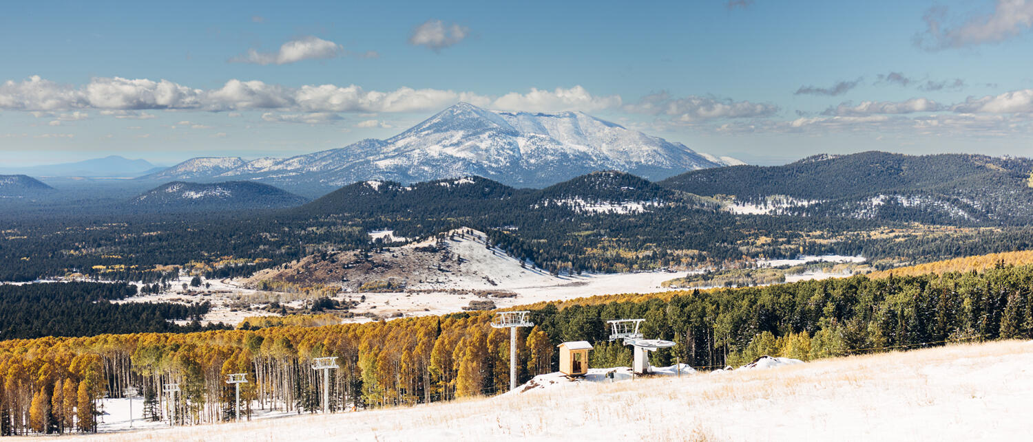 Landscape scene of snowy mountains in the distance and a snowy ski lift in the foreground.