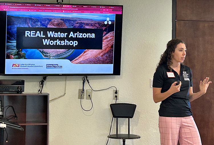 A woman stands in front of a screen talking to a room of people.