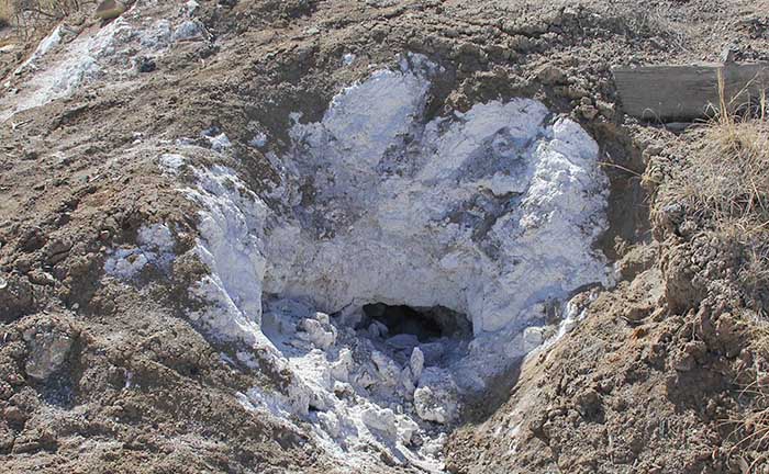A hole dug into a dirt hillside with a salt deposit.