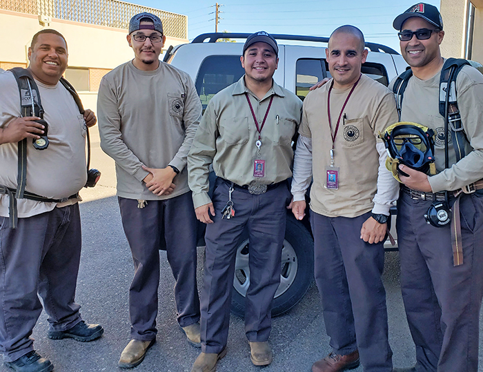 Five men in uniforms and with protective gear smile for a photo.