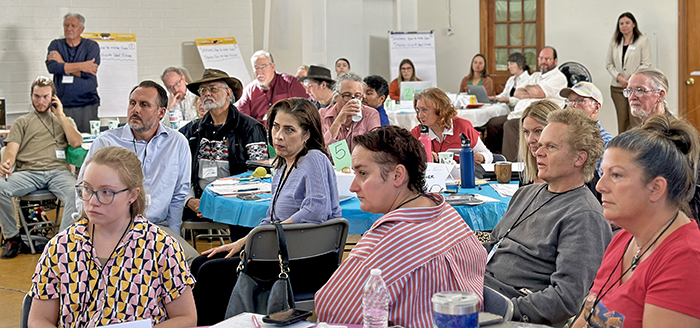 A large group of people sits at tables listening intently.