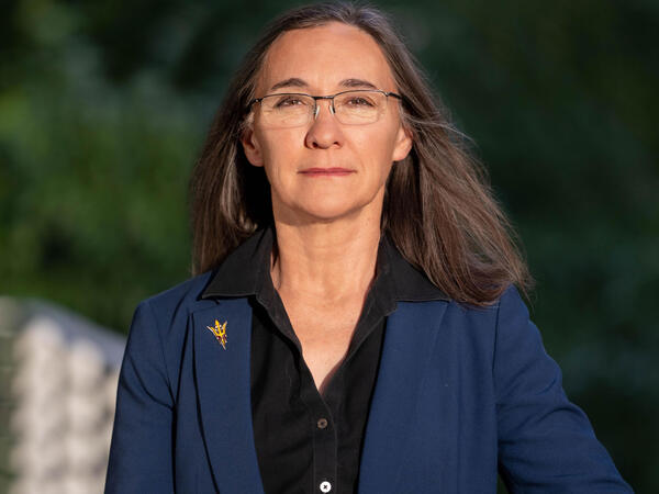 A woman with shoulder length brown hair in a blue jacket looks at the camera
