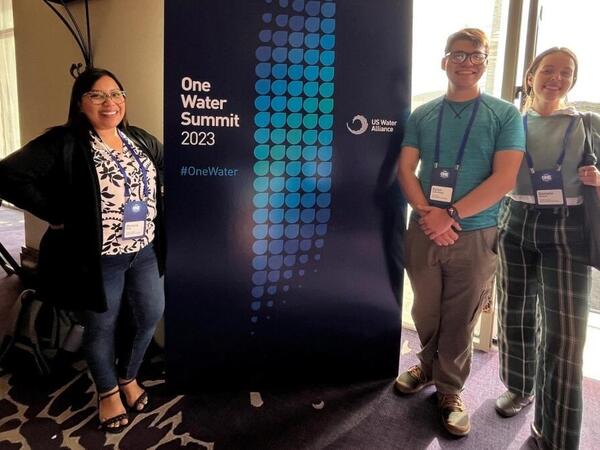 A group of three people stands in front of a conference sign