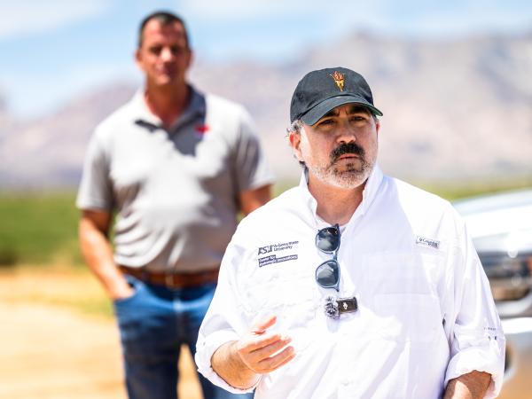 A man in a white shirt stands talking in a field.