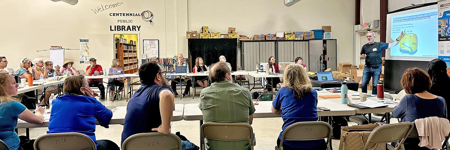 People gather around in a community space to listen to a speaker.